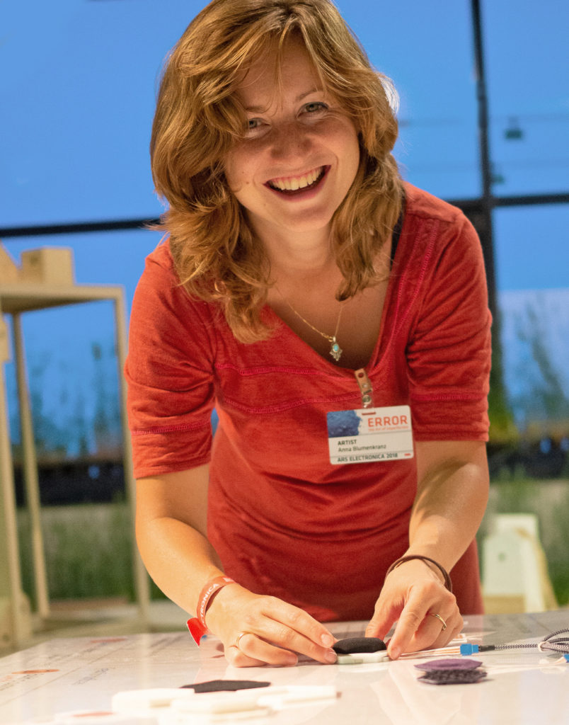 portrait of a woman in a red dress against blue background, bending over a table with sensors from a design research project